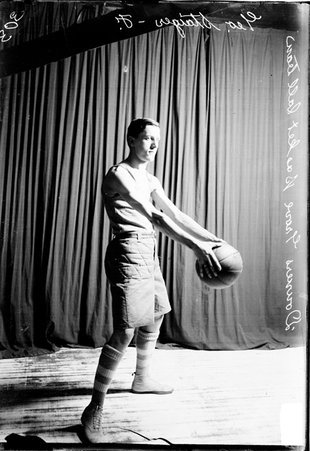Downers Grove basketball player George Staiger holding a basketball standing in front of a dark colored background - Chicago Daily News, Inc.