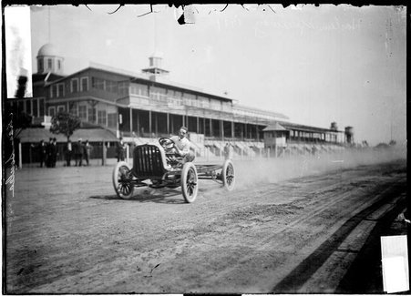 Motorist Charles Soules driving an automobile, with grandstands in the background - Chicago Daily News, Inc.