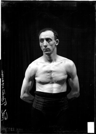 Wrestler, Ted Tunmann, looking to his right, standing in front of a dark backdrop - Chicago Daily News, Inc.