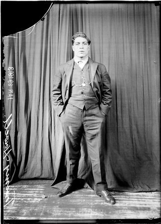 Pugilist, Tommy Howell, wearing a suit, standing in front of a dark backdrop - Chicago Daily News, Inc.