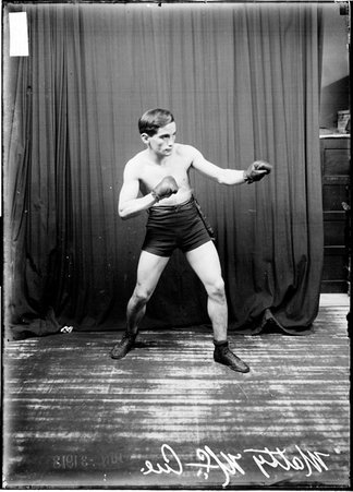 Pugilist, Matty McCue facing image right, standing in a boxing stance in front of a dark backdrop - Chicago Daily News, Inc.