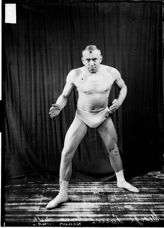 Wrestler, George Lurich, standing in a ready position in front of a dark backdrop - Chicago Daily News, Inc.
