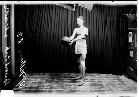 Basketball player, R. Miller, Seward Park, holding a basketball standing in front of a dark colored background - Chicago Daily News, Inc.