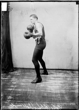 Pugilist, Willie Ritchie, facing image left, standing in a defensive boxing stance in front of a light-colored backdrop - Chicago Daily News, Inc.