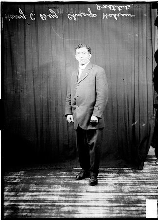 Wrestler, Harry Berz, wearing a suit, standing in front of a dark backdrop - Chicago Daily News, Inc.