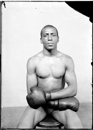 Boxer, Joe Gans, sitting in profile in front of a plain background in a room - Chicago Daily News, Inc.