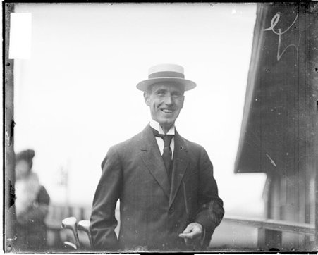 F. L. Finkenstaedt, holding a golf bag full of clubs, standing in front of a building - Chicago Daily News, Inc.