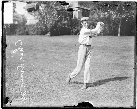 Golfer, Chick Evans holding a follow-through position, standing on the grounds of an unidentified golf club, dark exposure - Chicago Daily News, Inc.