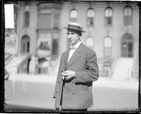Elmer Apperson, a automobile driver, standing outdoors Buildings are visible across the street in the background - Chicago Daily News, Inc.