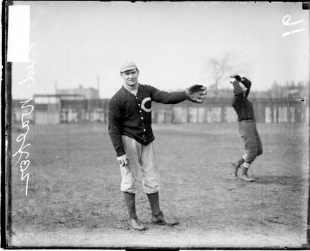 Fred Walker, coach of the University of Chicago baseball team, holding out his left arm, standing on an athletic field - Chicago Daily News, Inc.