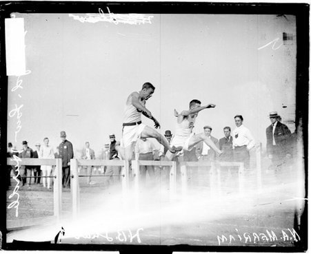 Athletes H.B. Shaw and Ned Merriam leaping over hurdles on an athletic track - Chicago Daily News, Inc.