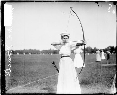 Archer Mrs. M. C. Howell holding a bow and arrow and pulling back the bow string - Chicago Daily News, Inc.