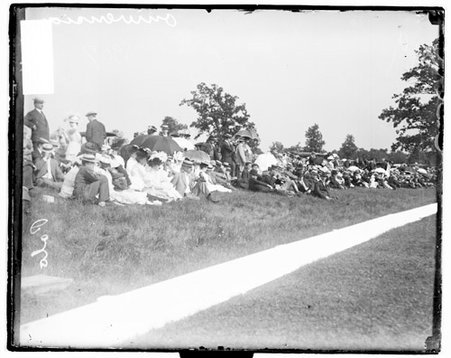 Spectators sitting and standing on a grassy hill on the sidelines of a polo field at Onwentsia Club - Chicago Daily News, Inc.