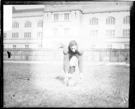 University of Chicago football player reaching towards a football lying on the ground - Chicago Daily News, Inc.