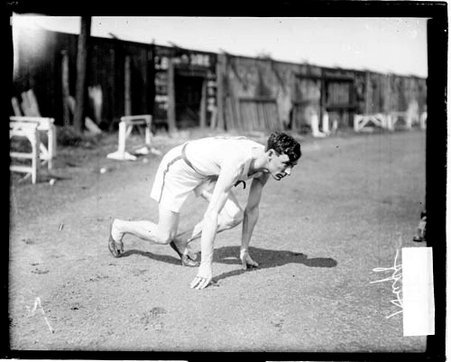 Runner Huff crouching in a ready position on an athletic track - Chicago Daily News, Inc.