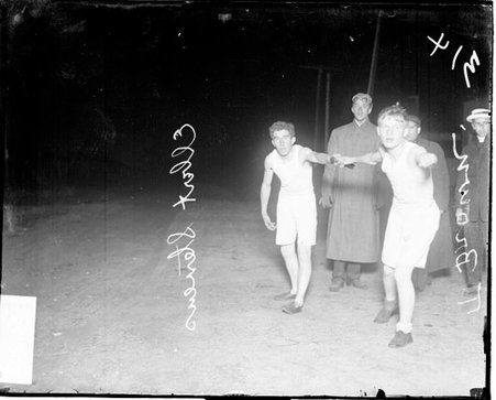 Runners E. Stevens and T. Brown holding on to a relay baton, standing outdoors at night - Chicago Daily News, Inc.