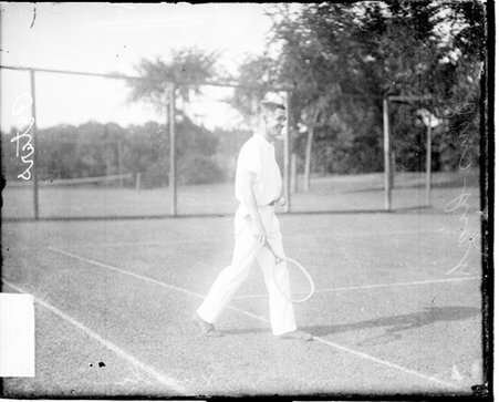Tennis player C. S. Peters holding a tennis racket, walking on a tennis court - Chicago Daily News, Inc.