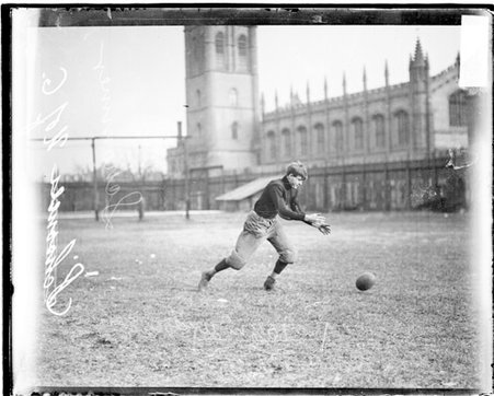 University of Chicago football player Schommer leaning forwards and looking at a football falling to the ground - Chicago Daily News, Inc.