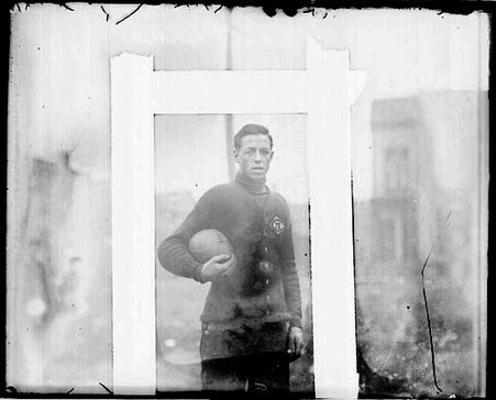 Football player Lane of Crane High School, holding a football, standing in front of a building - Chicago Daily News, Inc.