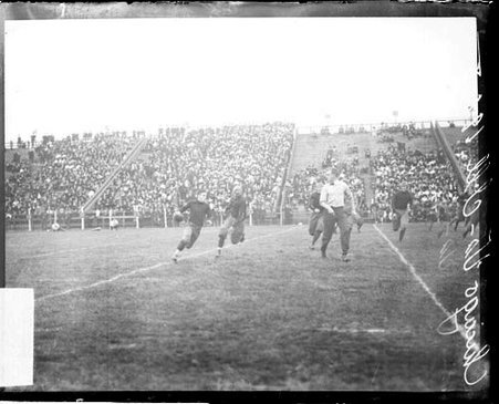 Unidentified football player holding a football running away from another unidentified football player on the field at Marshall Field - Chicago Daily News, Inc.