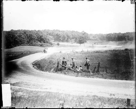 Group of spectators sitting and standing on the side of a curved dirt road during the Cobe Cup Race - Chicago Daily News, Inc.