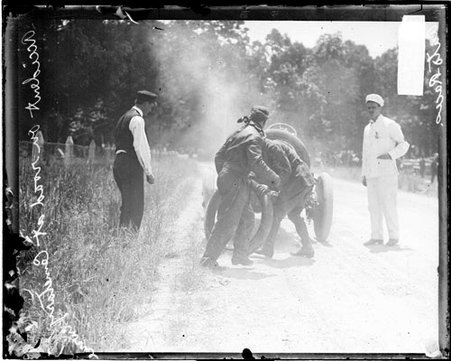 Two men standing behind an automobile parked on the side of a road, after an accident during the Cobe Cup Race - Chicago Daily News, Inc.