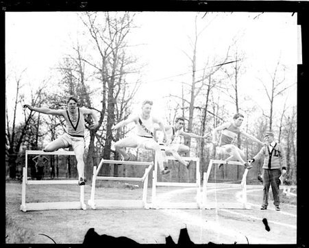 High school athletes Kuh, Jansen, and Llewellyn, leaping over hurdles on an athletic track - Chicago Daily News, Inc.