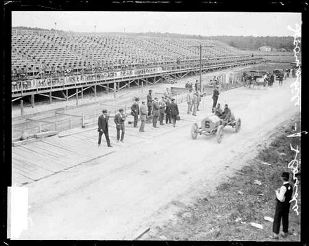 Automobile driver J. W. Florida and an unidentified man sitting in a Locomobile automobile parked on a road in front of bleachers during the Cobe Cup Race - Chicago Daily News, Inc.