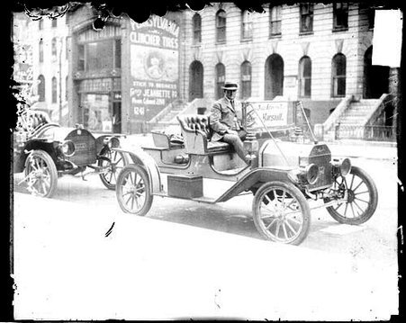 Unidentified automobile driver sitting in an automobile parked in front of another automobile along a sidewalk curb - Chicago Daily News, Inc.