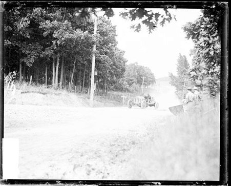 Unidentified man driving an automobile on a road bordered by trees on both sides - Chicago Daily News, Inc.