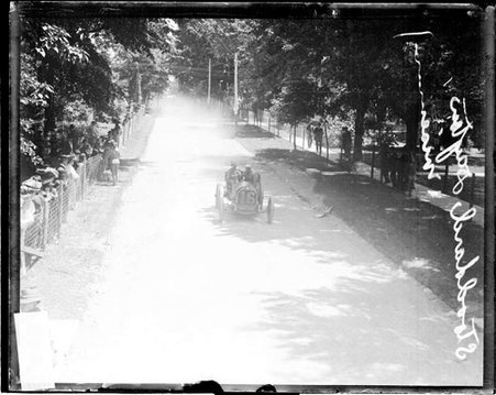 Automobile driver Wiseman driving a Stoddard-Dayton automobile, crowds are standing behind a fence along the side of the road - Chicago Daily News, Inc.