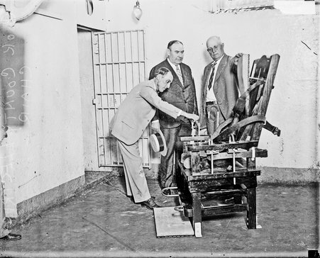 Three men standing next to an electric chair in the Cook County jailhouse - Chicago Daily News, Inc.