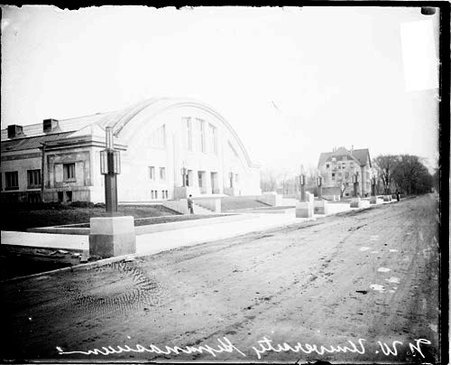 Northwestern University gymnasium located on the campus in Evanston, viewed at an angle from a muddy road in front of the building - Chicago Daily News, Inc.