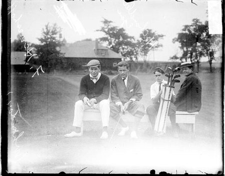 Golfers Fred Herreshoff and H. Chandler Egan sitting with a caddy on a bench at an unidentified golf club - Chicago Daily News, Inc.