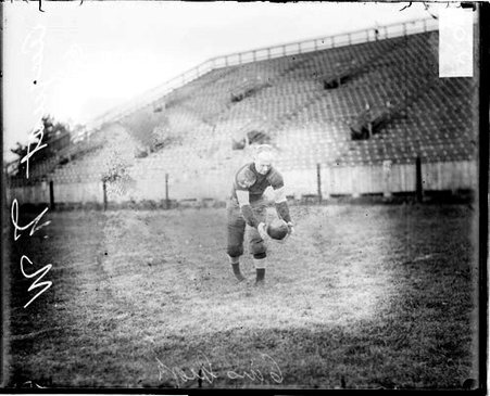 Northwestern University football player and captain Dave August leaning forward and holding a football - Chicago Daily News, Inc.