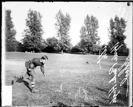 Hyde Park High School football player M. Smith holding a football and running in profile on an athletic field - Chicago Daily News, Inc.