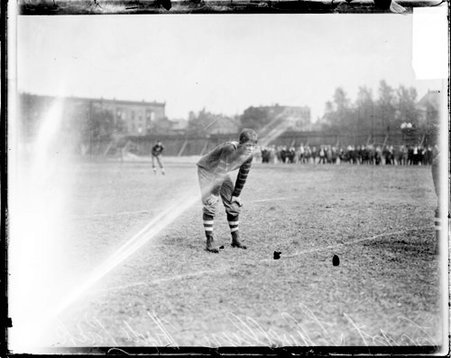 Hyde Park High School football player Llewellyn leaning forward with his hands on his knees on an athletic field - Chicago Daily News, Inc.