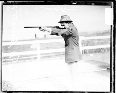 Shooter John Garrett aiming a rifle to the left of the camera, at the Chicago Gun Club - Chicago Daily News, Inc.
