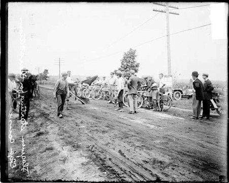 Group of men standing next to a row of motorcycles on a dirt road during an automobile race in Elgin - Chicago Daily News, Inc.
