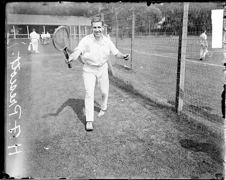 Tennis player H. F. Prescott holding a tennis racket, standing next to a fence separating rows of courts at the Aztec Tennis Club - Chicago Daily News, Inc.