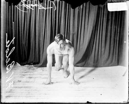 Athlete F. V. Belote crouching in a ready position in front of a dark backdrop - Chicago Daily News, Inc.