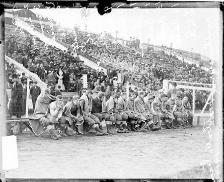 Members of the Northwestern University football team sitting on a bench in front of bleachers on the sidelines - Chicago Daily News, Inc.