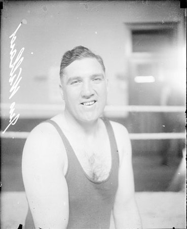 Boxer, J. Willard facing the camera, sitting in a boxing ring in a room - Chicago Daily News, Inc.