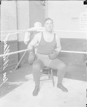 Boxer, J. Willard facing the camera, sitting in a corner of a boxing ring - Chicago Daily News, Inc.