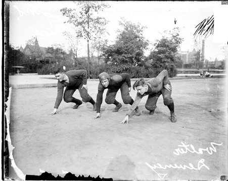 Wendell Phillips High School football players Deneney, Crist, and Koehler crouching in ready positions on a dirt field - Chicago Daily News, Inc.