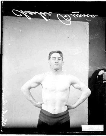 Wrestler Charlie Burns standing in front of a light-colored backdrop - Chicago Daily News, Inc.