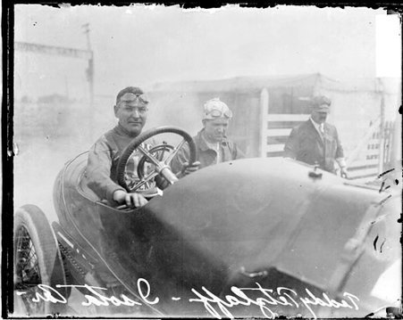 Automobile driver, Tetzlaff sitting in the driver's seat of an Isotta automobile parked in front of a structure and a wooden fence - Chicago Daily News, Inc.