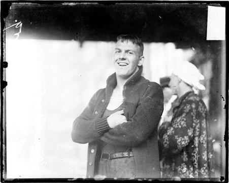 Swimmer William Vosburg wearing a sweater and pants over a bathing suit, standing in an open-air, covered area - Chicago Daily News, Inc.