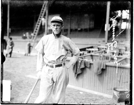 Baseball player, Evers, Cubs leaning against a baseball in front of grandstands on the field at West Side Grounds - Chicago Daily News, Inc.