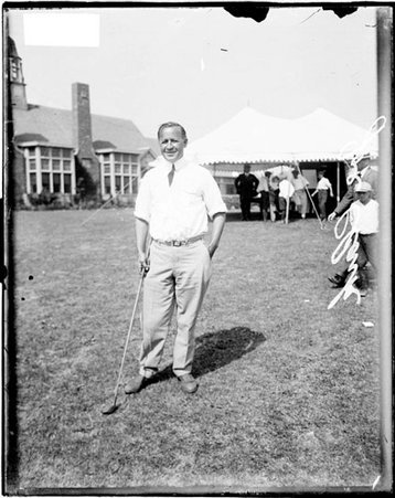 Golfer Joe Clark holding a golf club, standing in front of a building on the grounds of an unidentified golf course - Chicago Daily News, Inc.